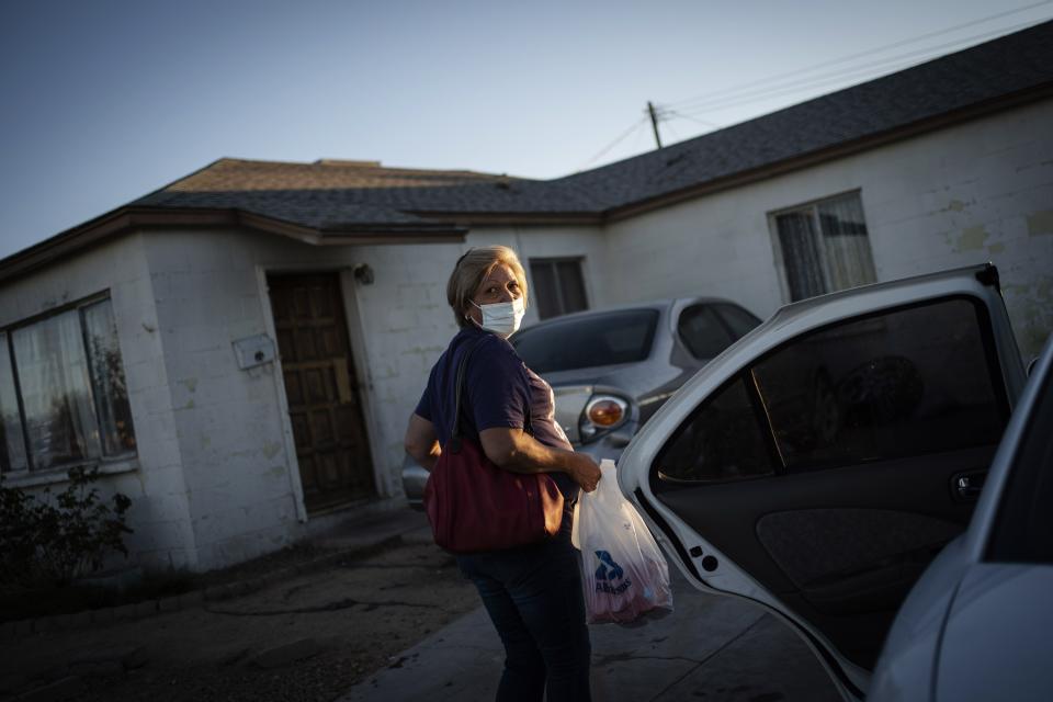 Norma Flores carries her groceries into her home in Henderson, Nev., Tuesday, Nov. 10, 2020. Flores is a Mexican immigrant who spent two decades working as a waitress at the Fiesta before COVID-19 descended and she lost her job. She lives in a concrete block house with six grandchildren, most of them doing school online. She dreads when she overhears a teacher asking what students had for their lunches and snacks. She rarely has enough food for both. (AP Photo/Wong Maye-E)