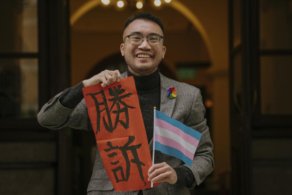 Transgender activist Henry Edward Tse holding a sign written 'Legal Victory' and a flag of transgender identity poses for a photograph outside of Court of Final Appeal in Hong Kong, Monday, Feb. 6, 2023. Hong Kong's top court ruled Monday that full sex reassignment surgery should not be a prerequisite for transgender people to have their gender changed on their official identity cards, in a move that is likely to have a far-reaching impact on the transgender community. (AP Photo/Anthony Kwan)