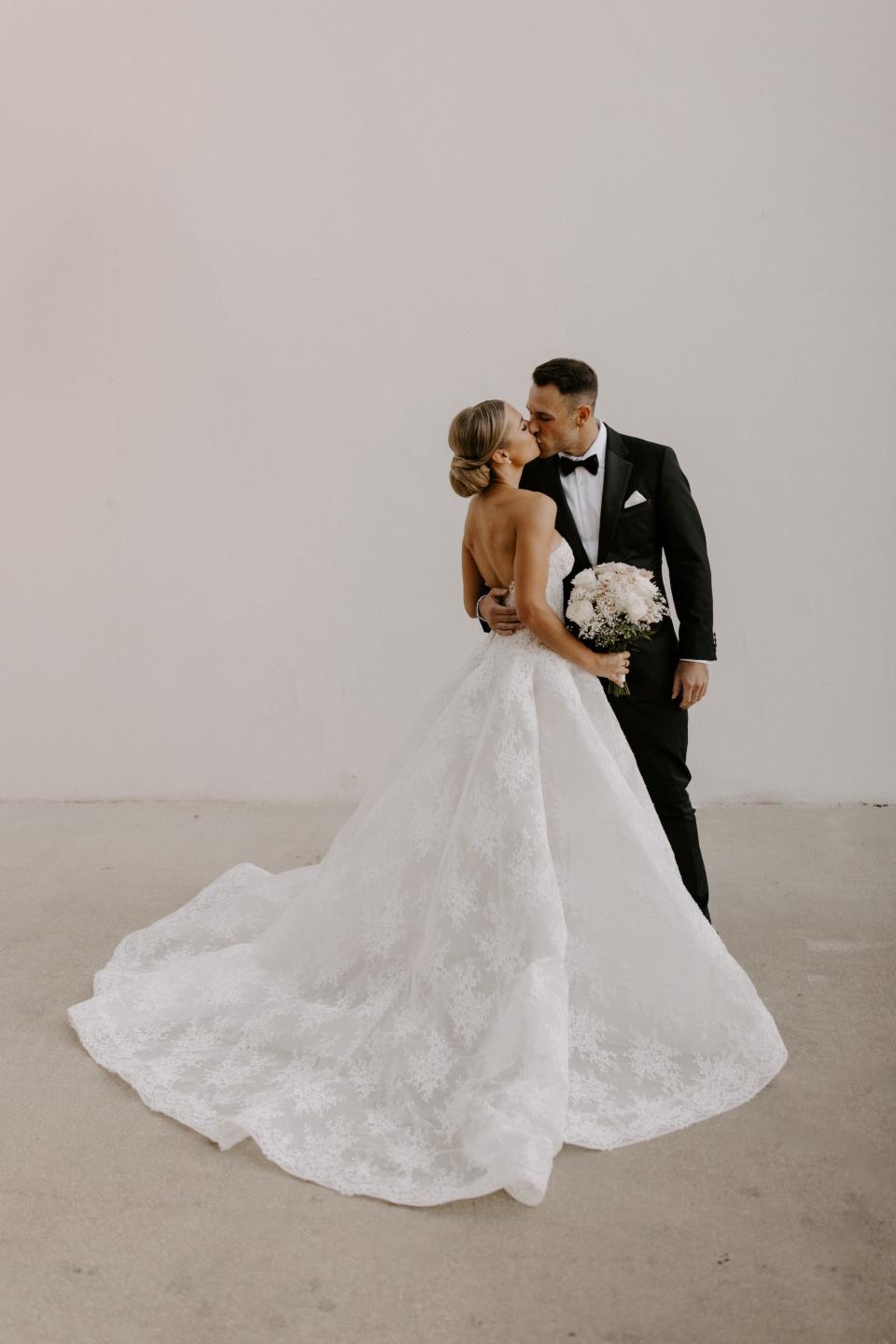 A bride and groom kiss in front of a white wall.