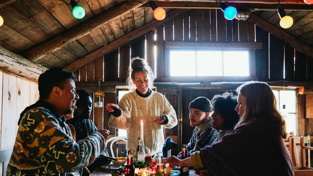 smiling young woman talking while enjoying meal with friends in cottage