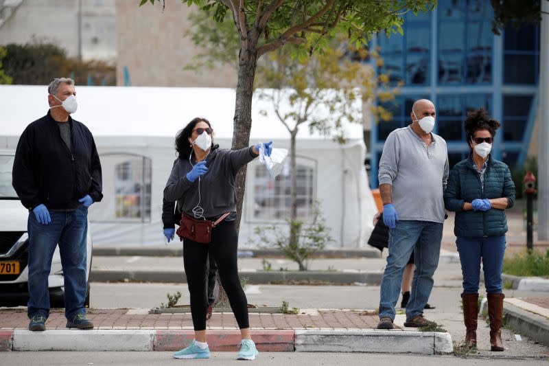 Israelis wearing masks and gloves stand next to a special polling station set up by Israel's election committee so Israelis under home-quarantine can vote, in Ashkelon