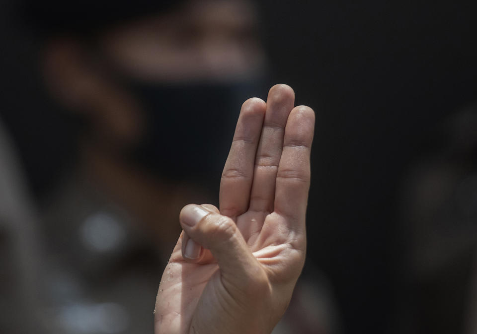 A pro-democracy supporter raises a three-finger salute, a symbol of resistance, in front of police officers at the Samranrat police station in Bangkok, Thailand, Thursday, Aug, 20, 2020. Thai police arrested a rapper and four pro-democracy activists in a crackdown on growing protests that have emerged as the most serious threat to the government led by a former army general they accuse of incompetence and corruption. (AP Photo/Sakchai Lalit)