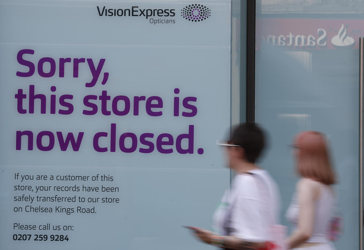 Pedestrians pass by a closed branch of Vision Express in Kensington, London, Wednesday, Aug. 12, 2020. The British economy is on course to record the deepest coronavirus-related slump among the world's seven leading industrial economies after official figures showed it shrinking by a 20.4% in the second quarter of 2020 alone said The Office for National Statistics. (AP Photo/Alastair Grant)