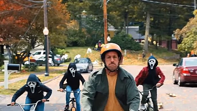 adam sandler as hubie rides a bike ahead of kids in ghostsface masks in a scene from hubie halloween a good housekeeping pick for best halloween movies