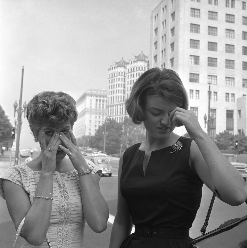 Two women with their hands near their eyes on a smoggy day in downtown Los Angeles, 1964.