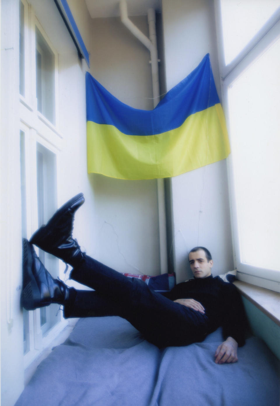 Morwan reclines in front of a Ukrainian flag that he hangs from his balcony (Photo credit: Nastya Platinova)