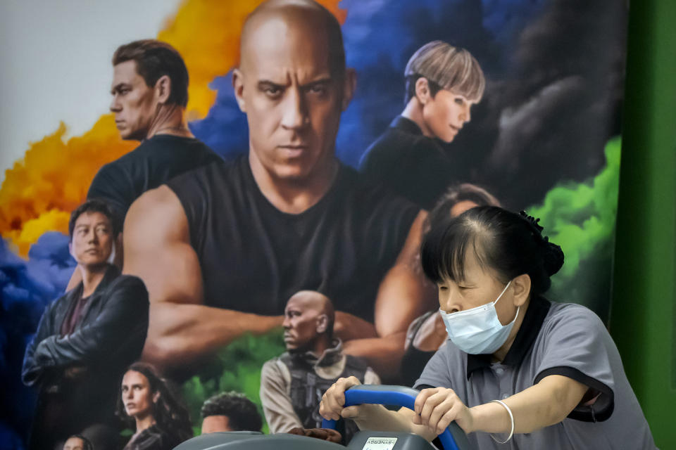 A worker pushes cleaning equipment past a poster for the movie "Fast & Furious 9" at a shopping mall in Beijing, Wednesday, May 26, 2021. Pro-wrestling champion and actor John Cena is apologizing after calling Taiwan a country in promotional interviews for his upcoming film "Fast & Furious 9." (AP Photo/Mark Schiefelbein)