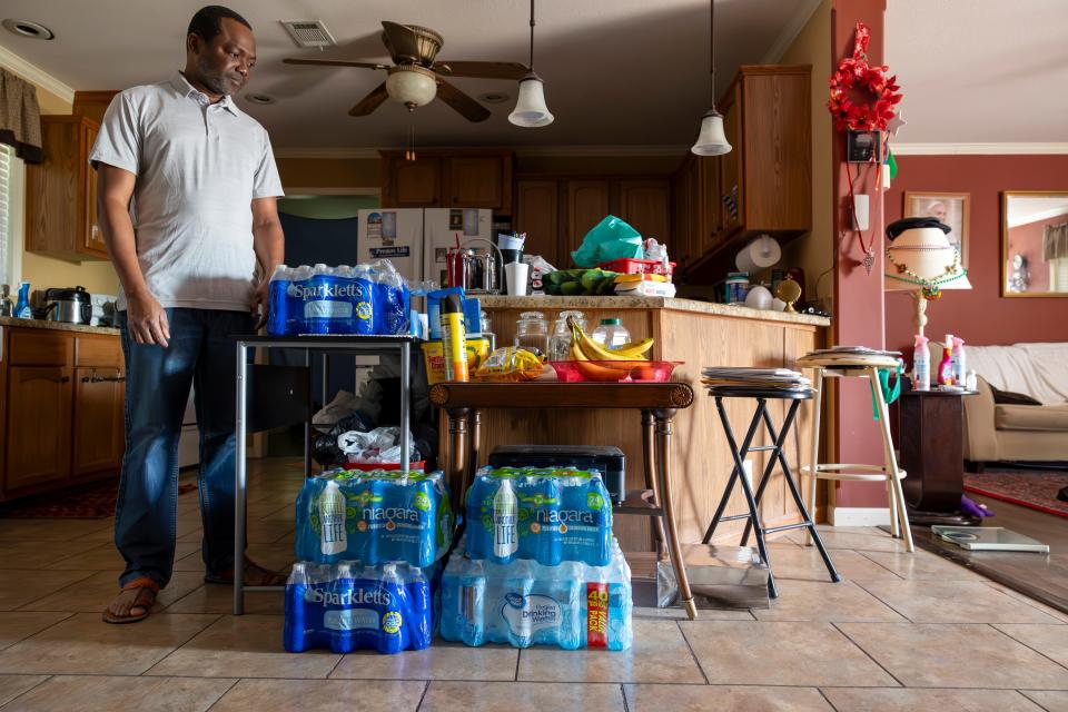 Rev. Sampson Abdulai, left, pastor of St. Thomas Catholic Church, stands in his kitchen next to extra containers of bottle water in Pointe a la Hache, La., on Friday, Sept. 29, 2023.