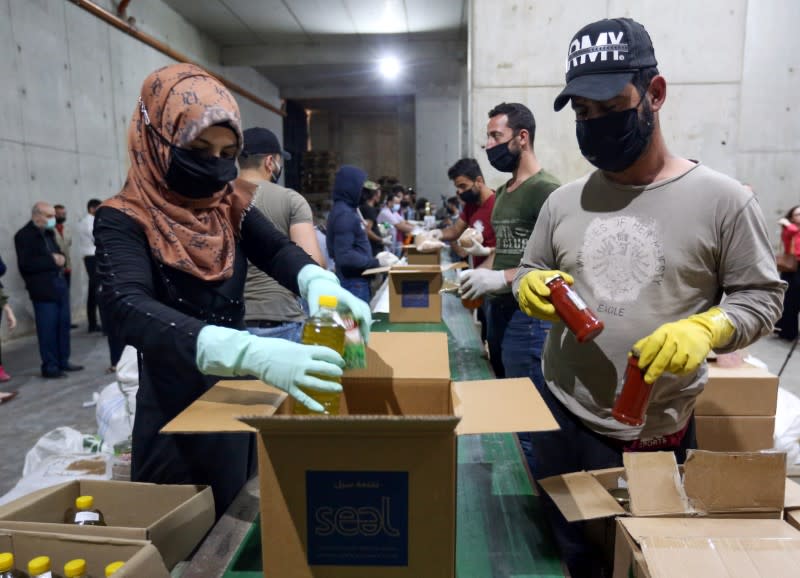 Volunteers wearing protective masks and gloves fill boxes with food for distribution to people in need, in Beirut