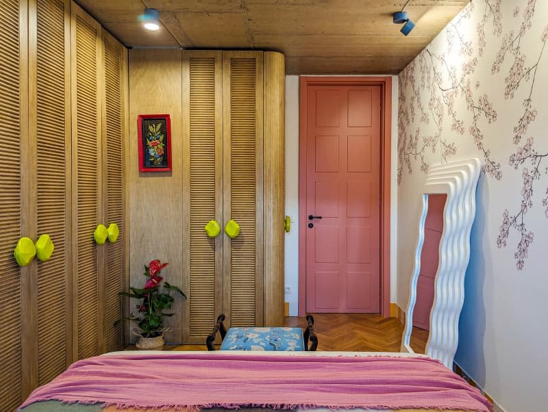 Bedroom with tree branch wallpaper wall, parquet wood floor, wall of wood closets, and pops of yellow and orange