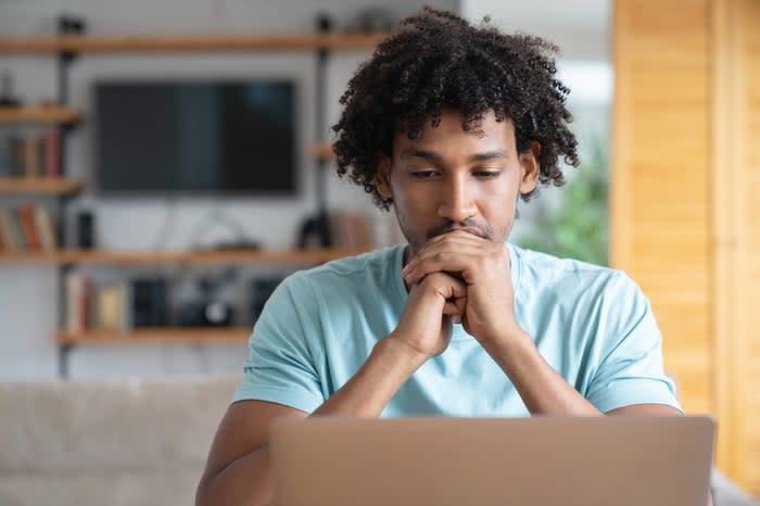 An investor thoughtfully looks at something on a laptop at home.