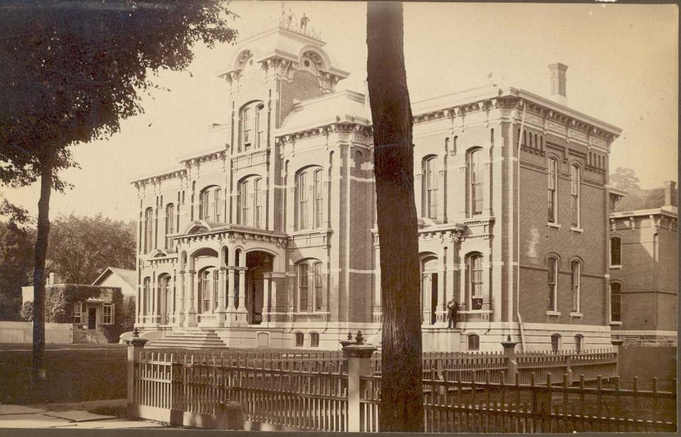 This view of the Wayne County Courthouse in Honesdale, circa late 19th or early 20th century, shows two men standing on top the belfry. Another stands outside at lower right with a fourth man looking out the window at lower right.