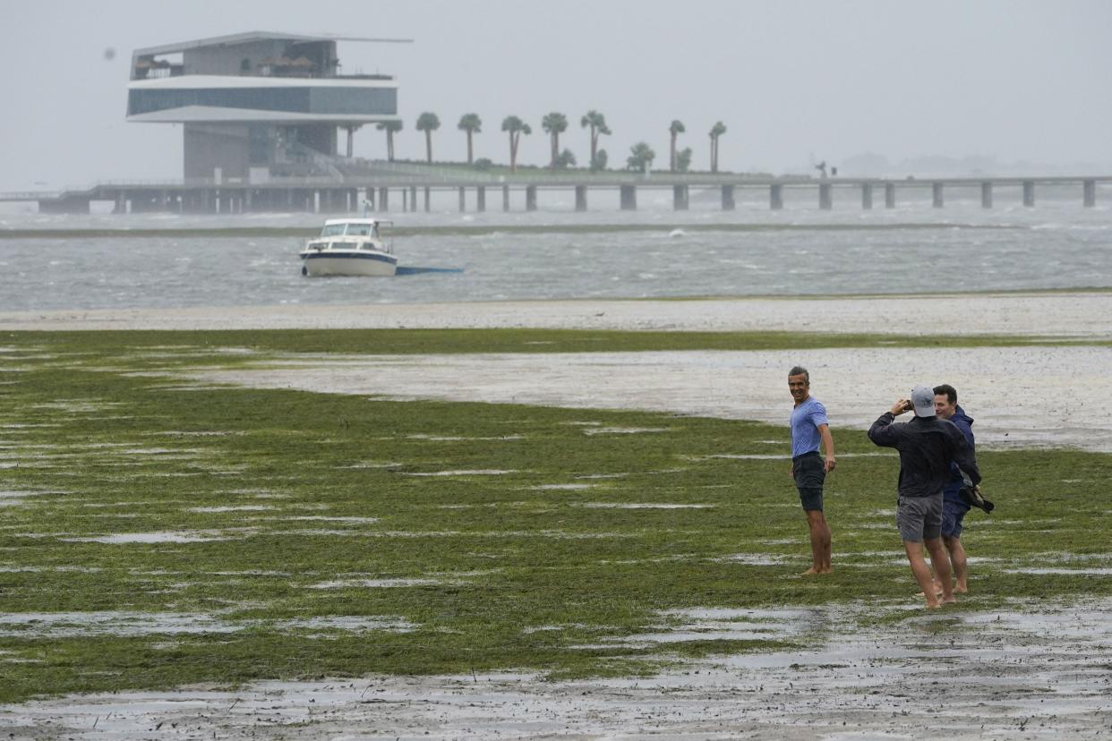 People walk where water is receding out of Tampa Bay due to a negative surge ahead of Hurricane Ian, Wednesday, Sept. 28, 2022, in Tampa, Fla.