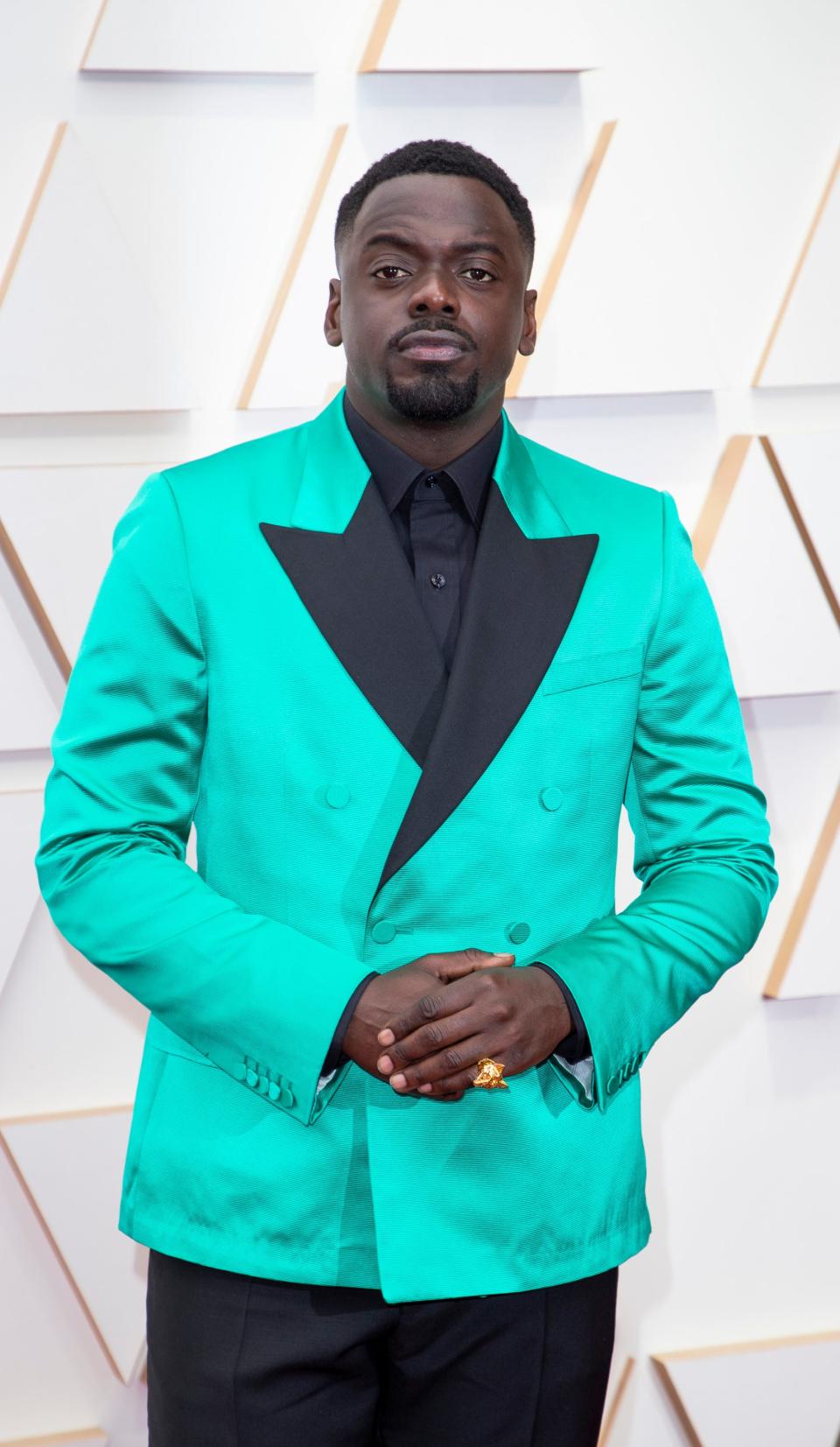 Daniel in a bright neon turquoise double breasted suit jacket with black lapels, a black shirt, and black trousers.