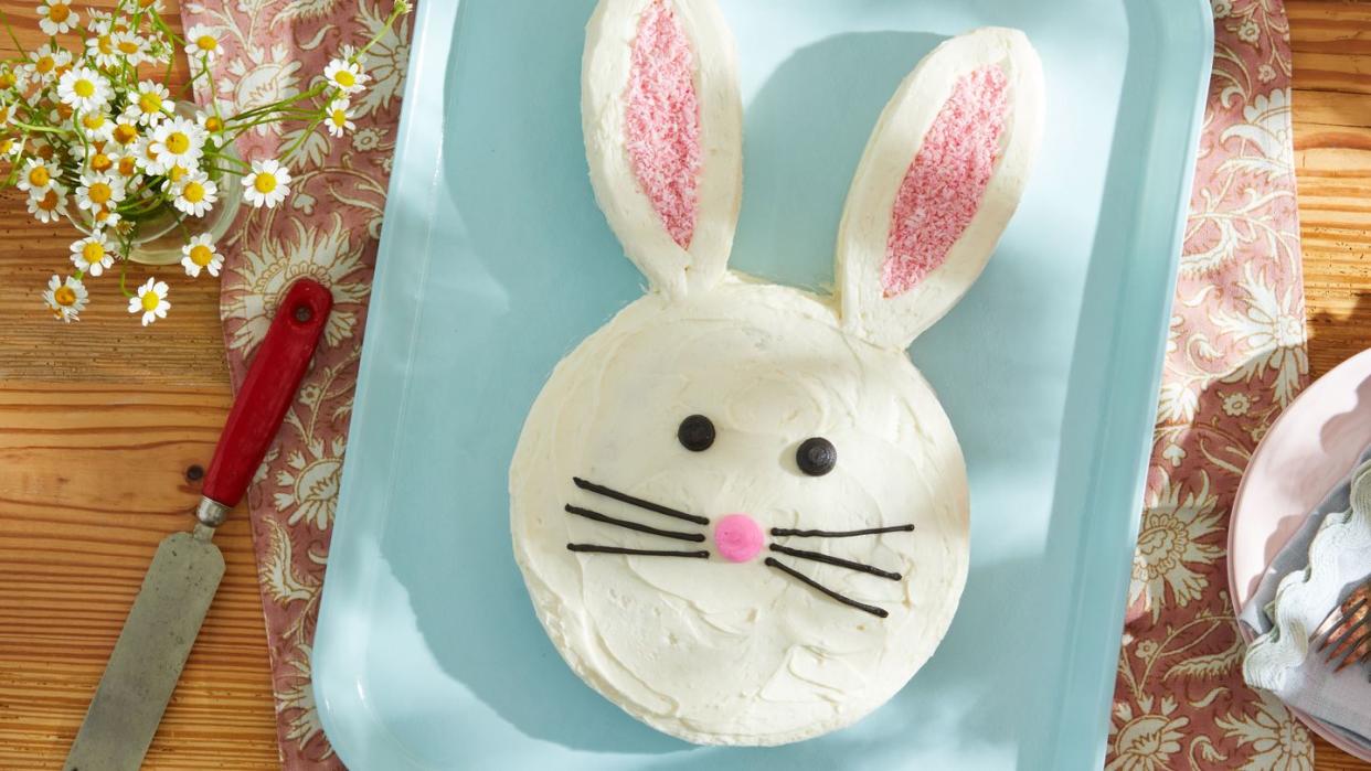 a single layer cake shaped like the easter bunny's head with tall ears and eyes and a nose and whiskers