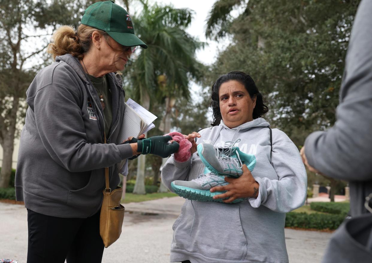 Tent City Helpers President Gail Harvey (left) gives shoes and socks to Monica Ocasio, who is experiencing homelessness, during a weekly food and supply distribution Monday, Jan. 8, 2024, at Memorial Park in Stuart. Hot meals from Stuart Church of Christ and supplies from Yaya Por Vida, a Port St. Lucie based nonprofit that helps people in recovery and active substance abuse, were also distributed.
