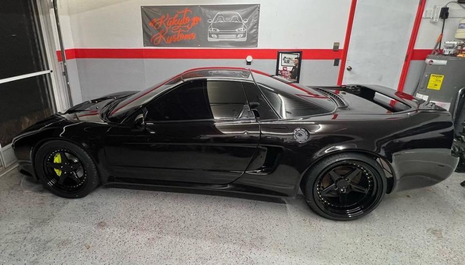 A black 1992 Acura NSX, shown from the side. The car is black with black wheels and a visible yellow front brake caliper. Its body has been widened.