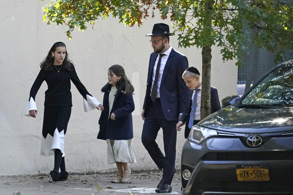 A man walks with his family, Sunday, Oct. 4, 2020, in the Borough Park neighborhood of New York. New York City's mayor says he has asked the state for permission to close schools and reinstate restrictions on nonessential businesses in several neighborhoods because of a resurgence of the coronavirus in nine zip codes, including Borough Park. Pending the governor's approval, shutdowns would happen starting Wednesday. (AP Photo/Kathy Willens)