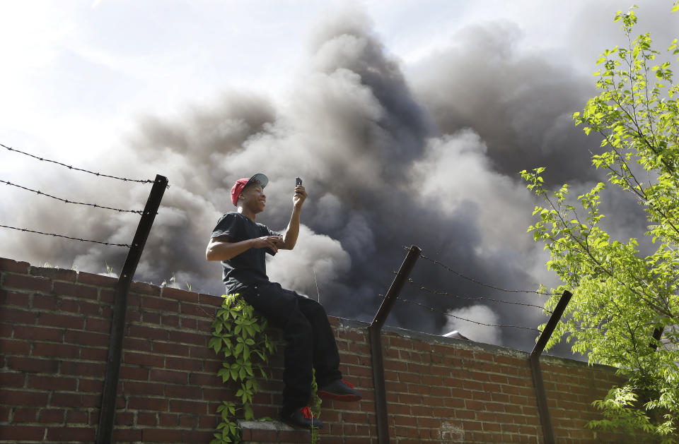 Deandre Wright takes a picture of himself as he watches a nearby commercial building burn near downtown Memphis, Tenn., on Saturday, April 26, 2014. Officials say four Memphis firefighters were rescued from the burning building after a wall collapsed on them. (AP Photo/Mark Humphrey)