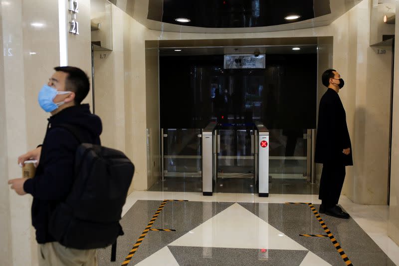 Men wearing face masks stand next to lines serving as a guide for social distancing, while waiting for the elevators at an office building, following an outbreak of the coronavirus disease (COVID-19), in Beijing