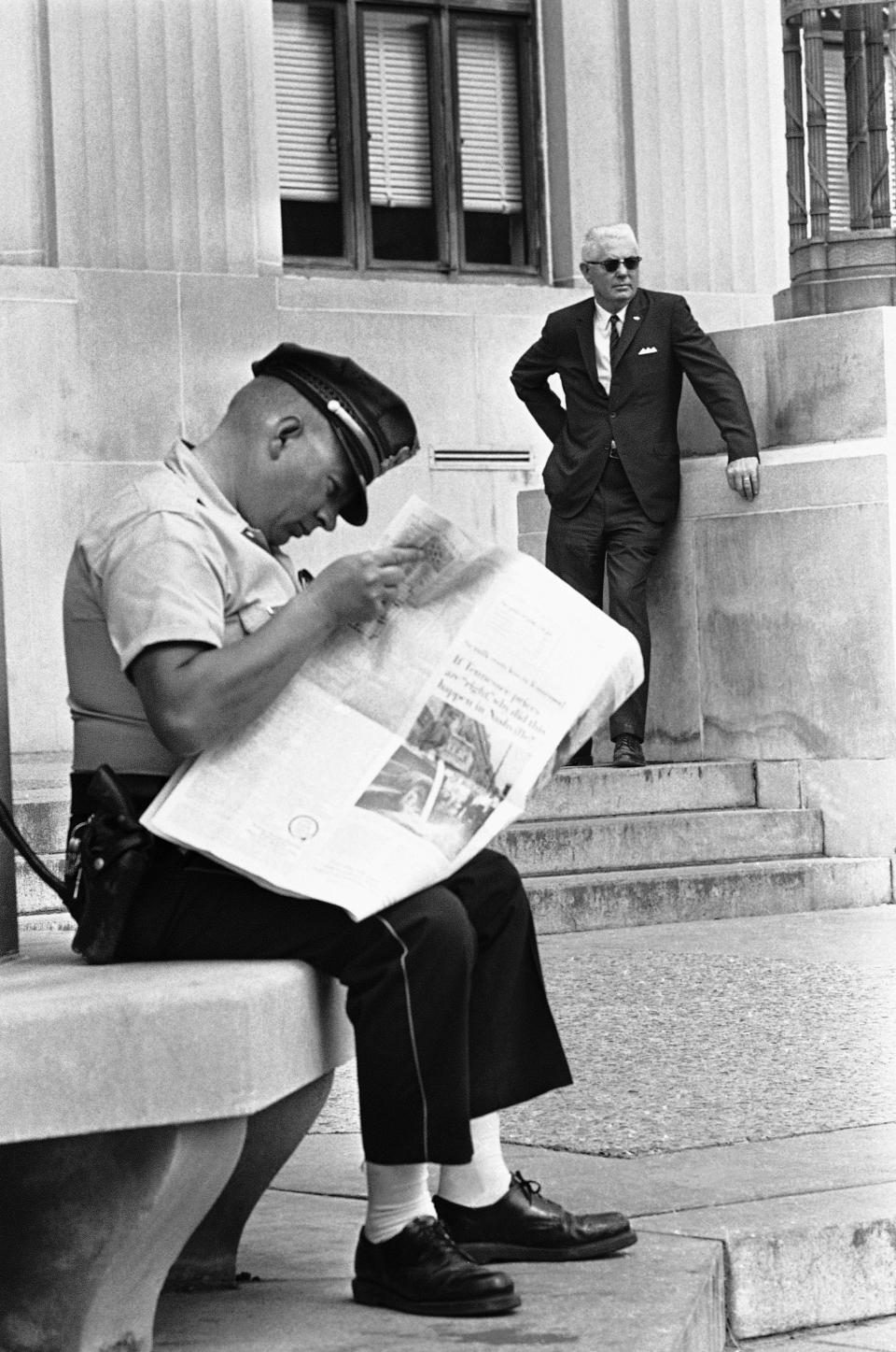 <p>A Meridian, Miss., policemen reads a newspaper containing stories about a trial of 18 white men charged with conspiracy in the slaying of three civil rights workers in 1964 outside the Federal building in Oct. 17, 1967 in Meridian, Miss., as Bernard Akin (background) looks on. Akin is one of 18 white men on trial in the case. (Photo: AP) </p>