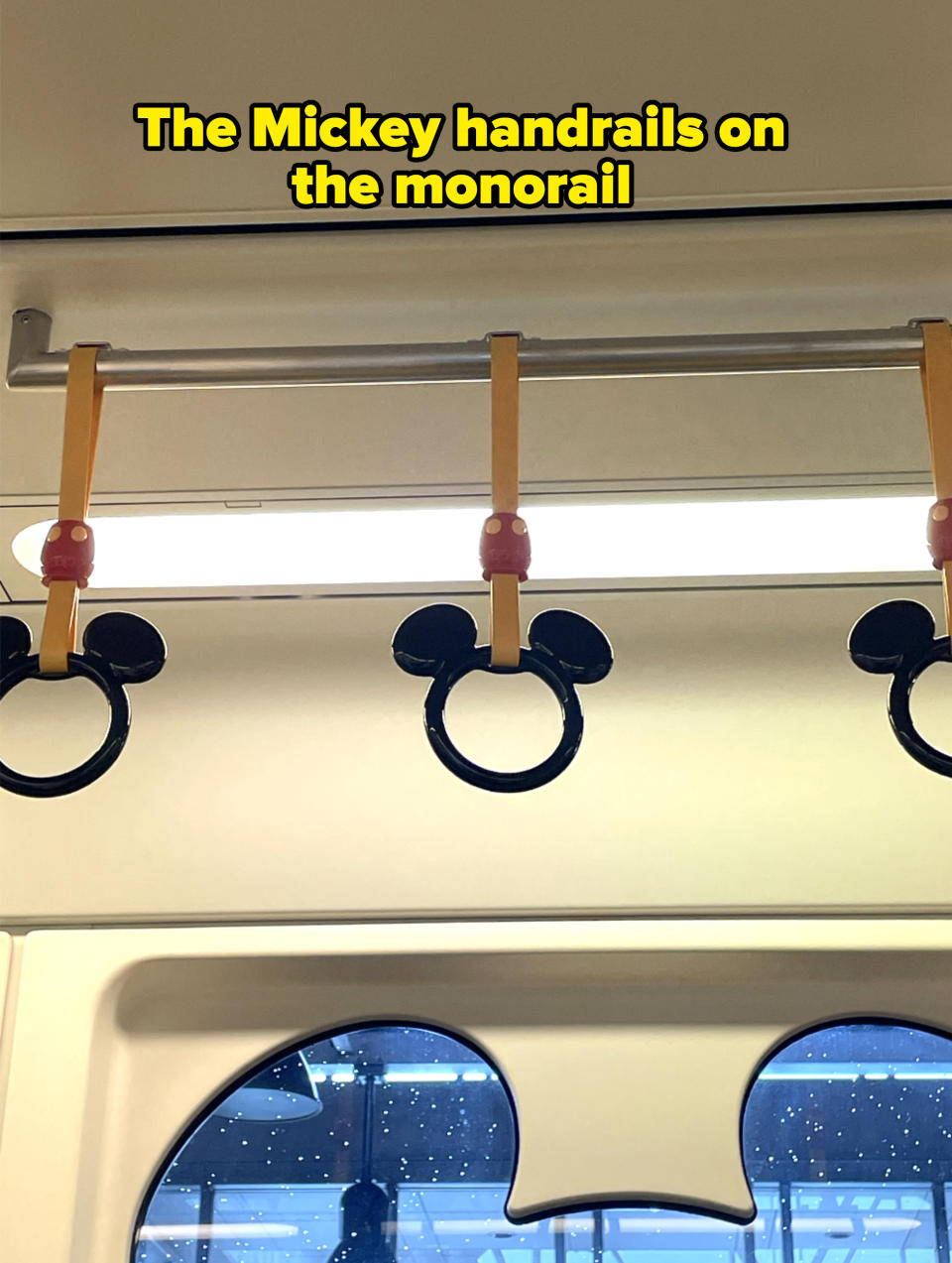 Hand grips shaped like Mickey Mouse ears with yellow straps are hanging in a vehicle, likely a train or bus