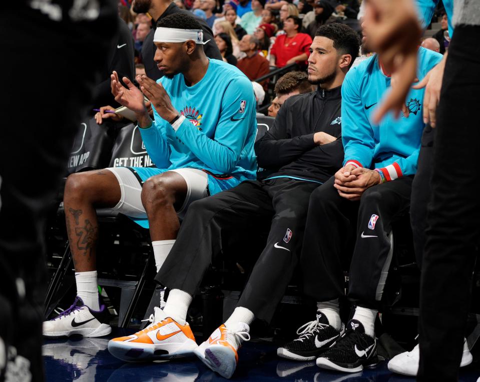 Phoenix Suns guard Devin Booker, wearing black, sits on the bench next to forward Torrey Craig in the first half of an NBA basketball game against the Denver Nuggets, Sunday, Dec. 25, 2022, in Denver. Booker, who was returning from an injury, played briefly in the first quarter before leaving the floor for the locker room and then returning to the bench. (AP Photo/David Zalubowski)