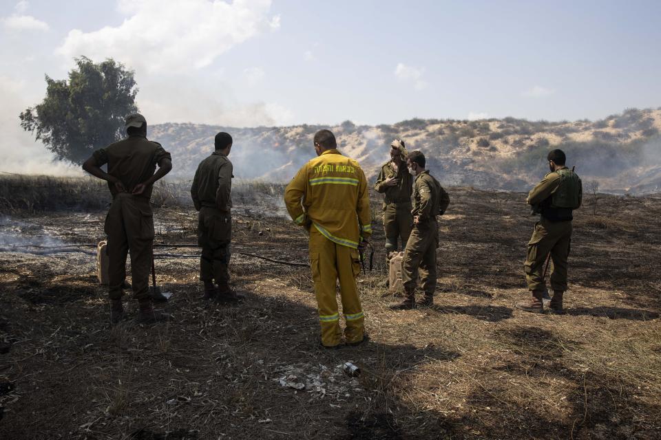 Israeli soldiers and a firefighter examine a fire started by an incendiary device launched from the Gaza Strip, on the Israeli side of the border between Israel and Gaza, near Kibbutz Netiv Ha'asara, Wednesday, Aug. 12, 2020. The Israeli military said it attacked a number of Hamas targets in the Gaza Strip early Wednesday in response to days of launches of explosives-laden balloons from Gaza into Israeli territory. Israel says it holds Gaza's Hamas rulers responsible for all fire emanating from the territory. (AP Photo/Tsafrir Abayov)