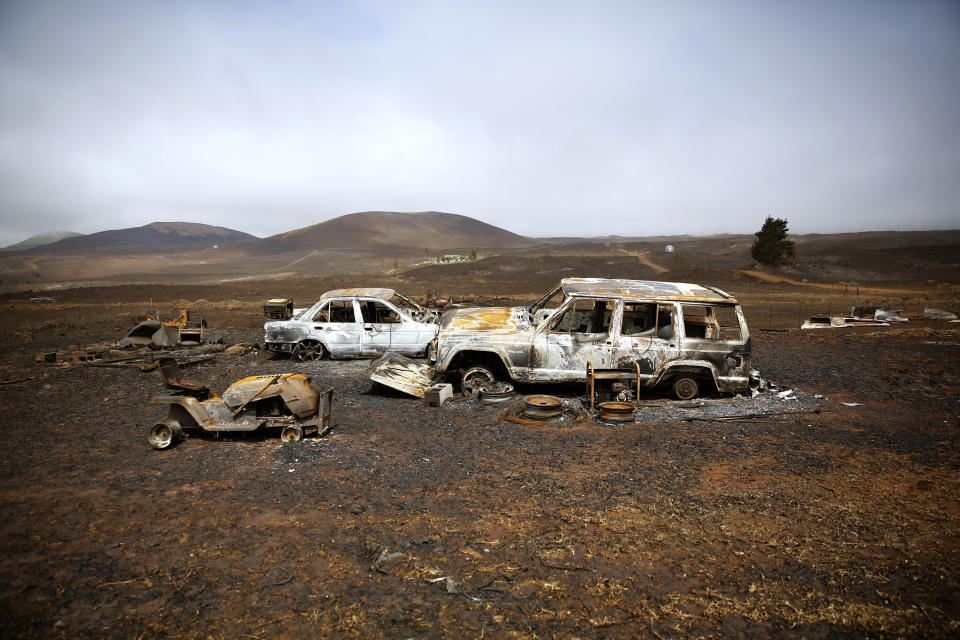 Vehicles destroyed by a wildfire sit on Joshua Kihe's property near Waimea, Hawaii, Wednesday, Aug. 4, 2021. The area was scorched by the state's largest ever wildfire. (AP Photo/Caleb Jones)