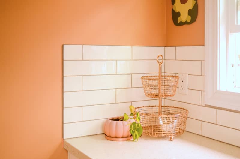 Corner view of accessorized countertop and white subway tile in orange kitchen.