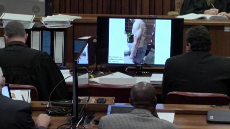 An image taken from the court pool TV via AP showing on screen a police photograph of Oscar Pistorius from the waist up and from the left side, showing blood on his shorts and parts of his body, with a tattoo visible on his back which was shown to the court in Pretoria, at his murder trial Friday, March 14, 2014. Prosecutors displayed two photos on TV monitors in the courtroom. A second photo shows him standing on his blood-stained prosthetic legs and wearing shorts covered in blood, taken shortly after the athlete fatally shot his girlfriend. The photographs were taken in the garage of Pistorius’ Pretoria home where the athlete killed Reeva Steenkamp in the early hours of Valentine’s Day, 2013, a former policeman testified. (AP Photo/Court Pool via AP)