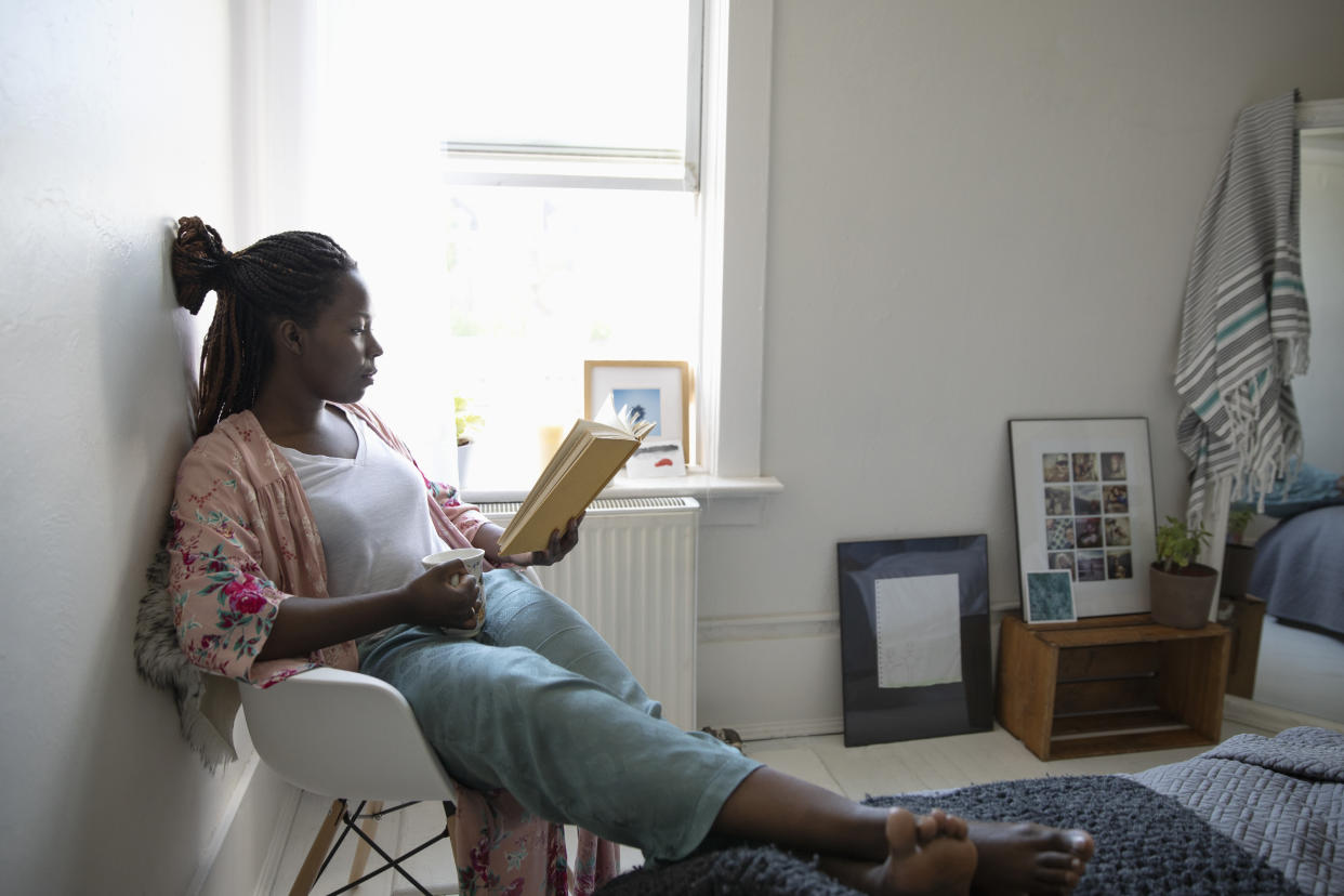 Young woman relaxing, drinking coffee and reading book in bedroom