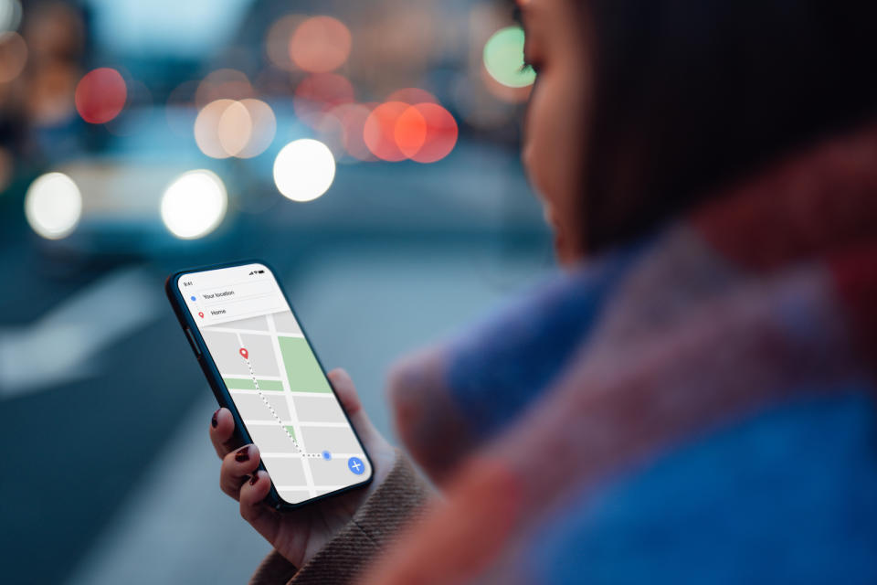 Over the shoulder view of woman using GPS navigation app on smartphone to navigate and search for location in city. Travel and navigation concept. Hand holding mobile phone mockup.