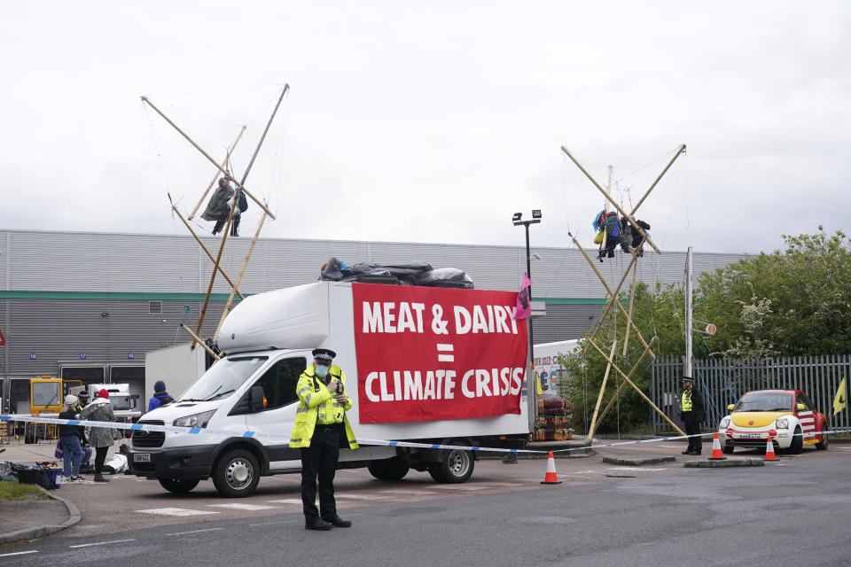 Animal Rebellion protesters suspended from a bamboo structure and on top of a van, being monitored by police officers outside a McDonald's distribution site in Hemel Hempstead, England, Saturday May 22, 2021. Animal rights protesters are blockading four McDonald’s distribution centres in the U.K. in an attempt to get the burger chain to commit to becoming fully plant-based by 2025. Animal Rebellion said Saturday that trucks and bamboo structures are being used at the distribution sites in Hemel Hempstead, Basingstoke, Coventry and Heywood, Greater Manchester, to stop lorries from leaving depots. (Yui Mok/PA via AP)