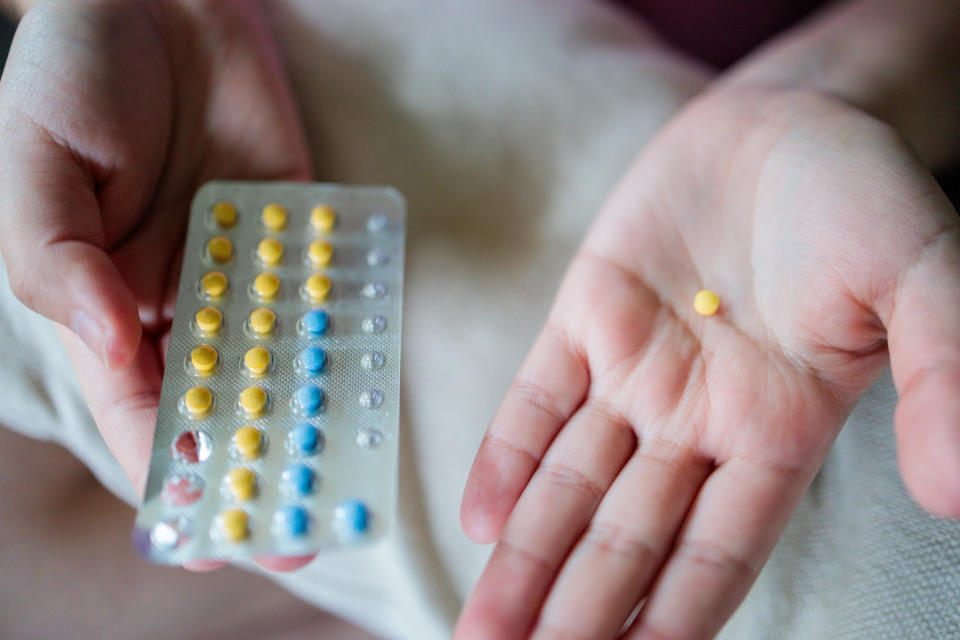 A person's right hand holds a blister pack of pills while the left hand holds a single pill