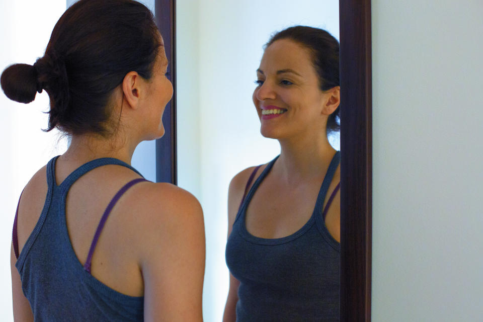 Woman smiling at herself in the mirror. (Getty Images)