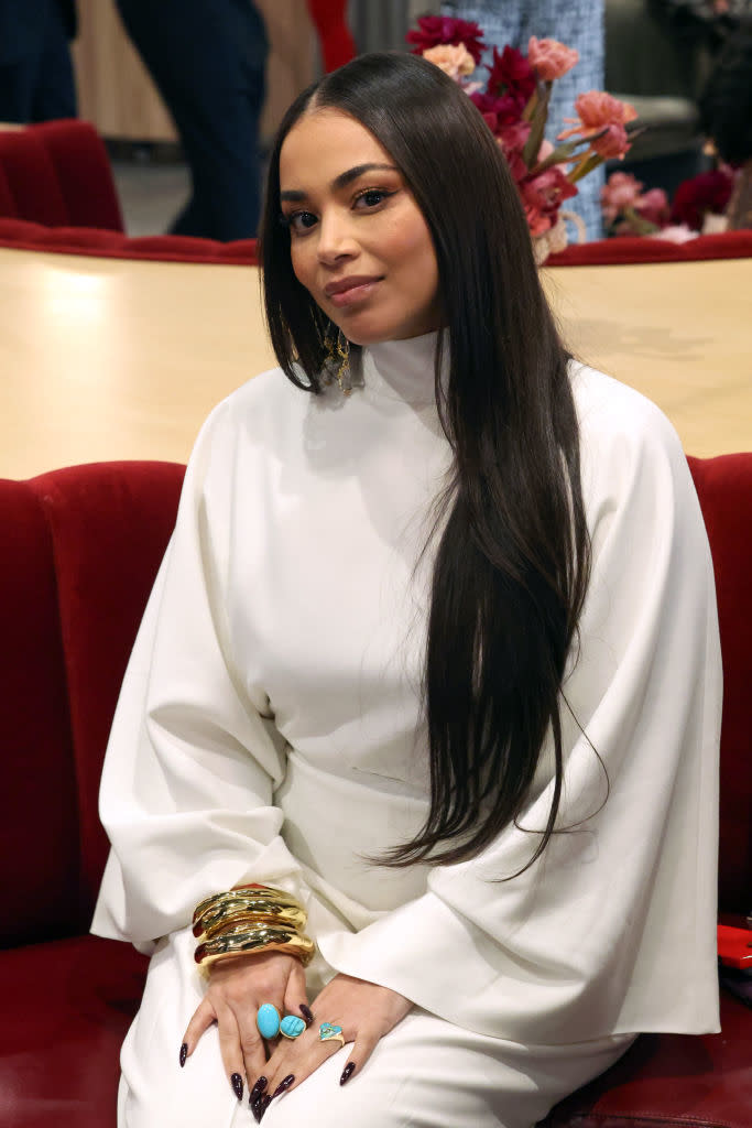 Lauren London seated, wearing a turtleneck with long sleeves and layered bracelets