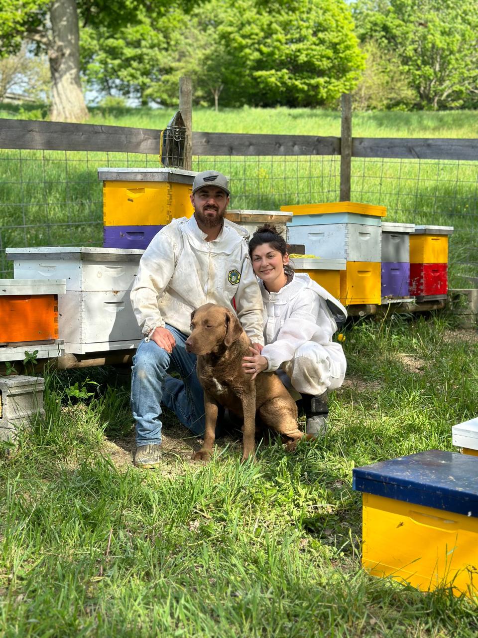 Chad and Brittany Edwards with their dog Koda in front of bee hives they are using to collect honey.