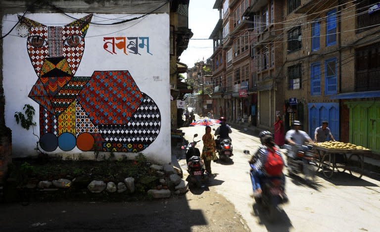 Nepalese travel past a mural in Kathmandu on August 20, 2013. Nepal's capital has been given a facelift thanks to a team of artists who have painted dozens of elaborate and metres-high murals on walls around the Himalayan city