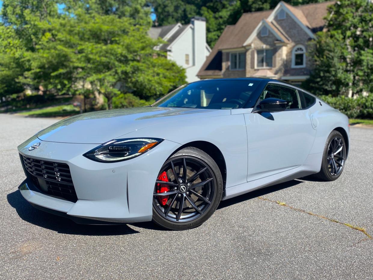 A gray 2024 Nissan Z Performance with black wheels and red brake calipers is parked in front of homes.