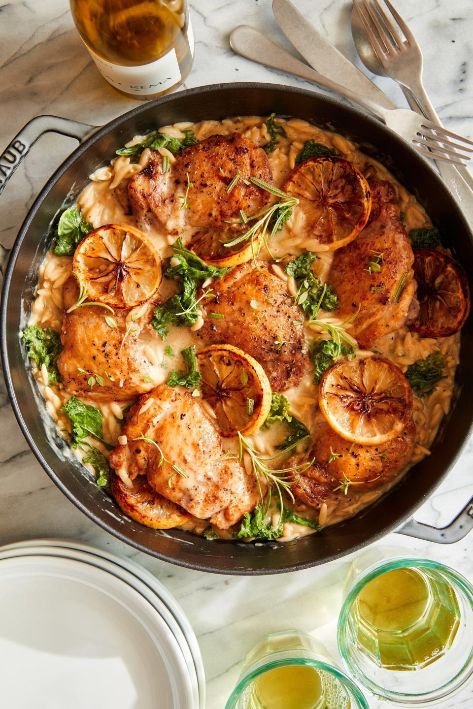 Skillet with chicken, herbs, and slices of lemon, served with drinks on the side. Perfect for a gourmet meal feature