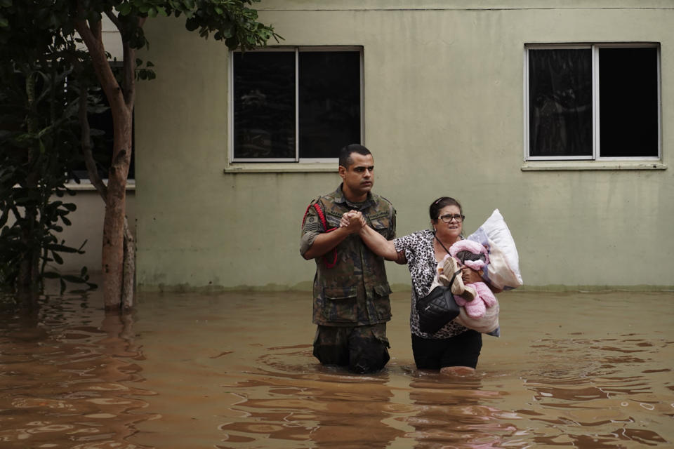 A soldier helps a woman evacuate from a neighborhood flooded by heavy rains, in Canoas, Rio Grande do Sul state, Brazil, Saturday, May 4, 2024. (AP Photo/Carlos Macedo)