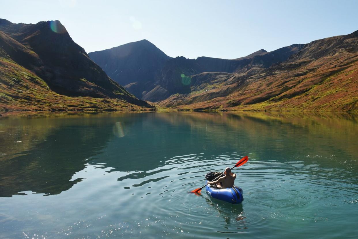 Destinations that make for perfect Cool Weather Summer Vacations. Pictured: man riding on kayak surrounded by mountains.