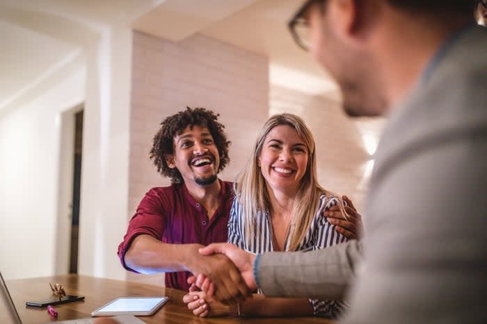 A couple happily shakes hands with a real estate agent in an office.