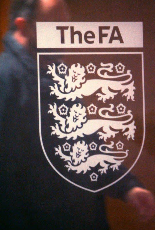 A man passes behind engraved logo on glass door entrance to Football Association headquarters in central London