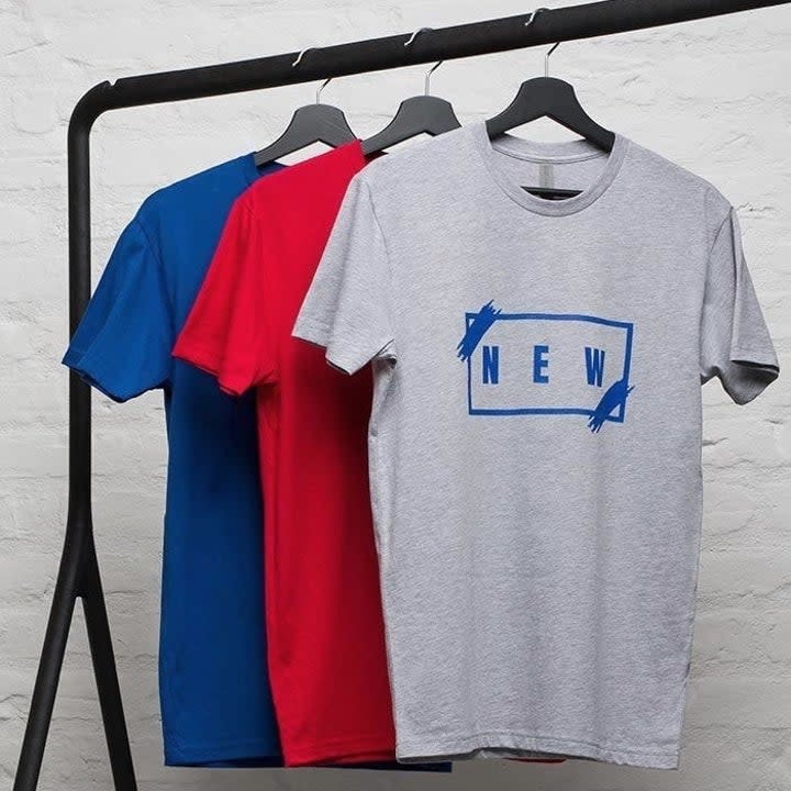 a rack with three T-shirts in different colors hanging on it with the front-most one featuring a graphic that says 