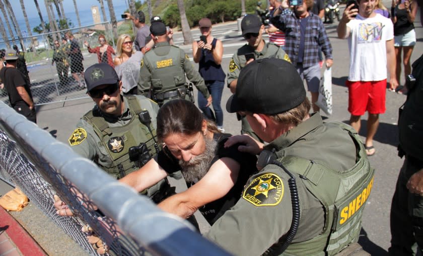 With sheriff&#39;s deputies holding him in place, Alan Hostetter clings to a fence at the Pier Bowl parking lot on May 21, 2020, as part of a rally he organized to demonstrate against the fencing around the lot.