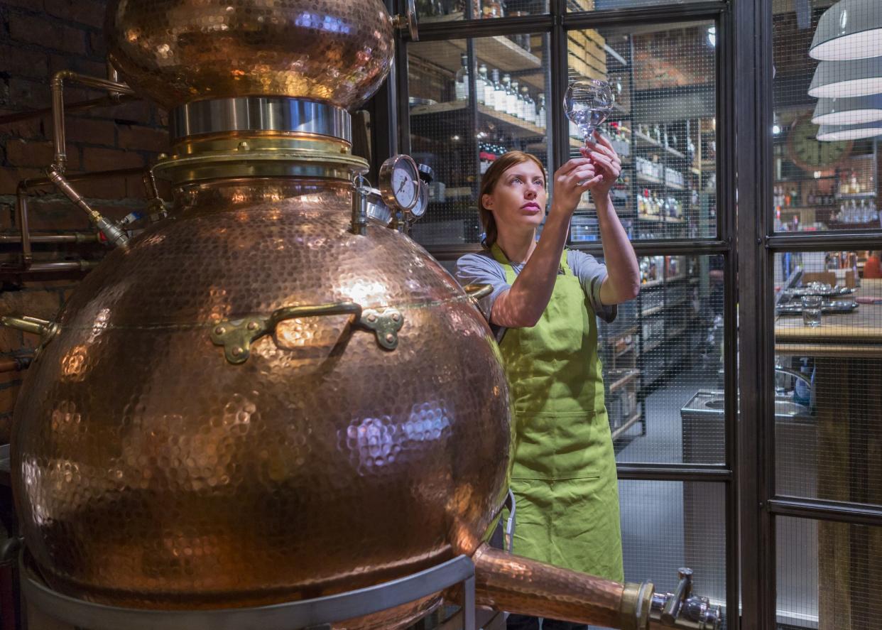 A female worker is sampling the alcohol produced from the copper distillery boiler. It is used to produce Gin and Whiskey.