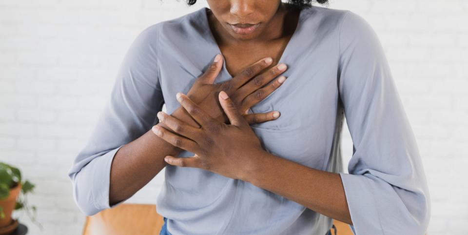 young adult woman looks down, closes her eyes, and puts her hand on the pain in her chest