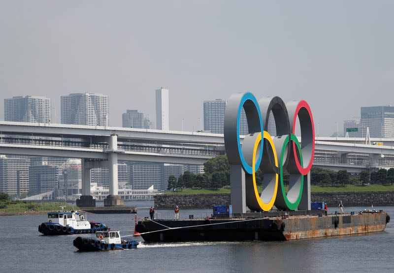 Boats tow the giant Olympic rings, which are being temporarily removed for maintenance, at the waterfront area at Odaiba Marine Park in Tokyo